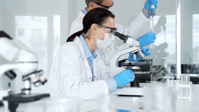 Researchers working in a modern laboratory, performing scientific experiments with a microscope and test tubes, analyzing samples for biology and medical breakthroughs