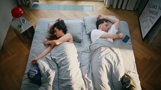 Overhead couple relaxing in bed browsing phone together at cozy home morning