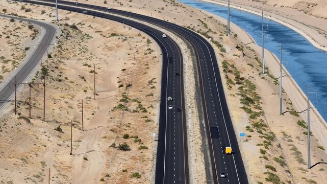 Highway running parallel to a long water canal through a dry sandy landscape, high-angle aerial view