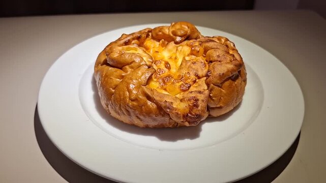 freshly baked golden-brown cheese bread or pastry sitting on a clean white ceramic plate under warm indoor lighting.