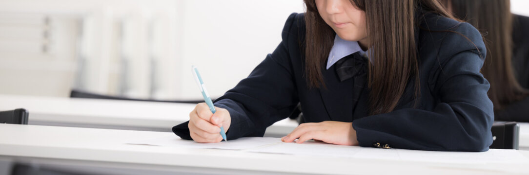 教室で真剣にテストに取り組む日本人女子高校生複数　受験、定期テスト、模試の学生　顔無しのバナー手元のクローズアップ