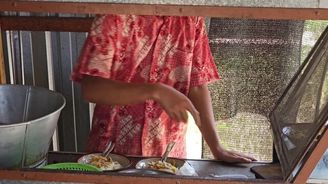 Street food vendor in a red batik shirt serving traditional Indonesian dishes with a lime wedge at a local food stall