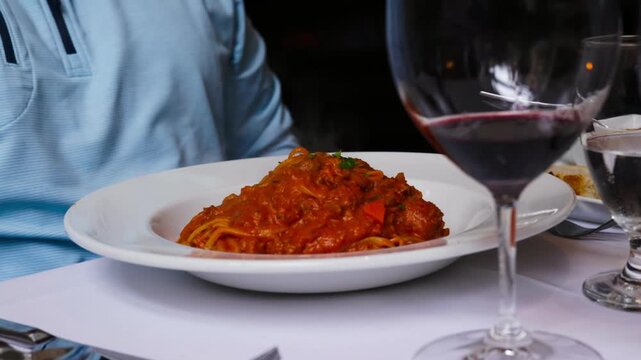 Spaghetti bolognese and red wine on restaurant table, static shot