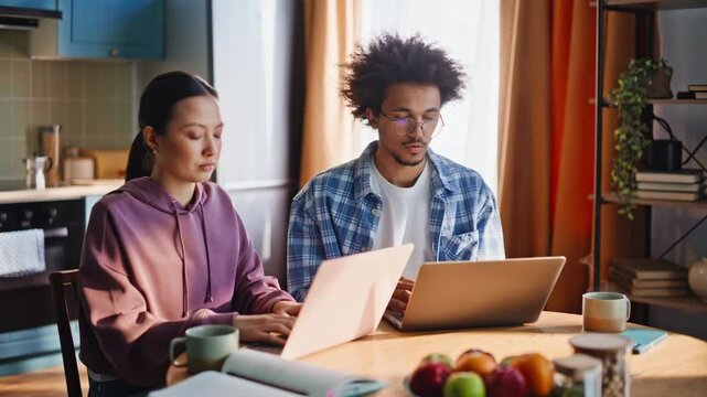Multiethnic couple working laptops home. Man frustrated by bad news online.