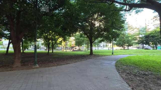 Walking POV on a paved curved pathway in a green summer park, 4K b-roll