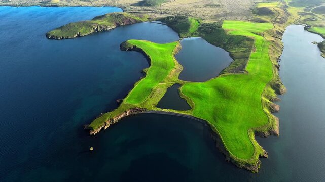 Oblique aerial motion of green peninsula with inland lakes and surrounding blue coastal waters captured from high viewpoint showing shoreline geometry and field contours