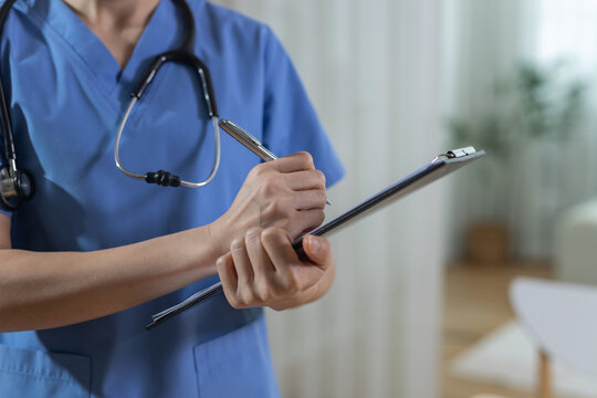 medical professional doctor or nurse wearing healthcare scrub writing on clipboard with stethoscope around neck in clinic environment showing diligent caring attitude during assessment