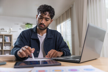 Obraz premium man working on digital tablet with stylus pen and laptop computer at home office desk with serious expression studying business chart document