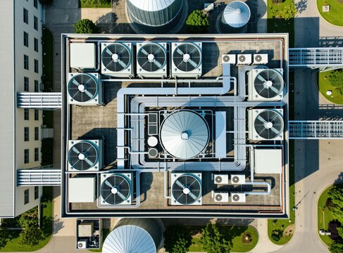 Aerial view of industrial building rooftop featuring large HVAC units, complex piping systems. Complex mechanical infrastructure for climate control provides cooling, ventilation for facility. Many