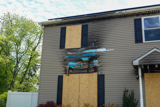 An abandoned fire damaged house with boarded windows and solar panels on its roof, set in a suburban environment. The atmosphere conveys neglect and damage. The scene is well-lit with a clear sky.