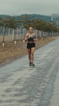 Wide shot of female runner approaching down open road toward hills