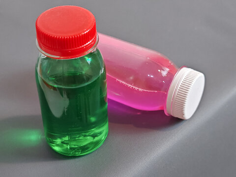 a standing bottle with green liquid and a lying bottle filled with translucent pink fluid. Designed for use in commercial laboratory product demonstrations, chemical analysis stock themes, or retail