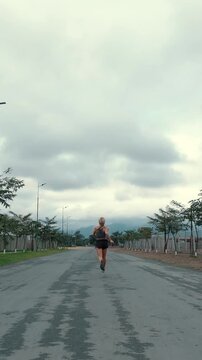 Back view of female runner receding down a long straight road