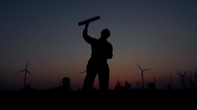 Silhouetted wind turbine technician conducts equipment inspection amidst towering turbines and dusky twilight sky-isolated industrial scene for renewable energy solutions.
