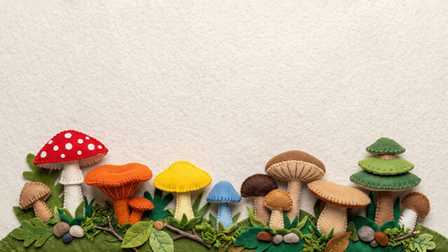 Colorful handcrafted felt mushrooms and leaves arranged along the bottom against a textured white background with copy space, ideal for charming kitchen decor.