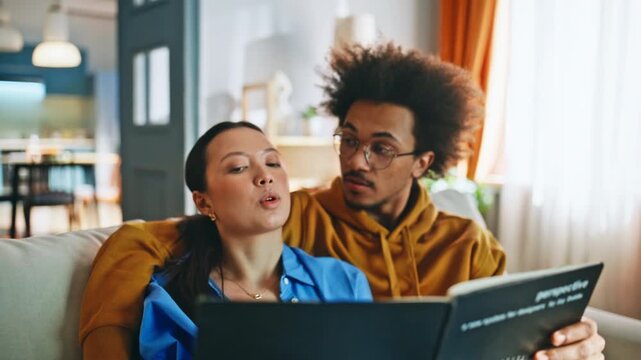 Couple browsing photo album on sofa. Closeup of pair sharing memories at home.