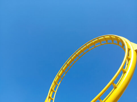 Yellow roller coaster track loop against a clear blue sky