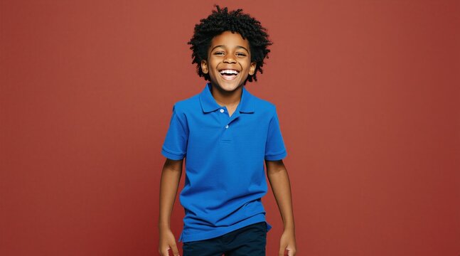 Happy young Black boy laughs in blue polo shirt on plain red background. Curly hair kid has joyful expression and is full of fun. Positive child face, energetic mood.
