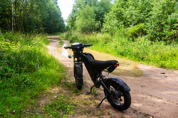 Modern black electric bike parked on a muddy rural path surrounded by lush summer greenery, adventure vibes with a rugged e-bike ready for off-road trail riding in nature © PhotoChur
