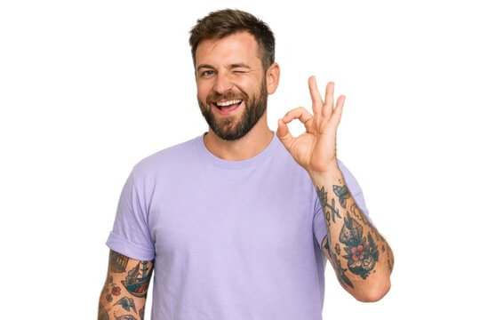 Smiling man winking with OK gesture, tattooed arms.