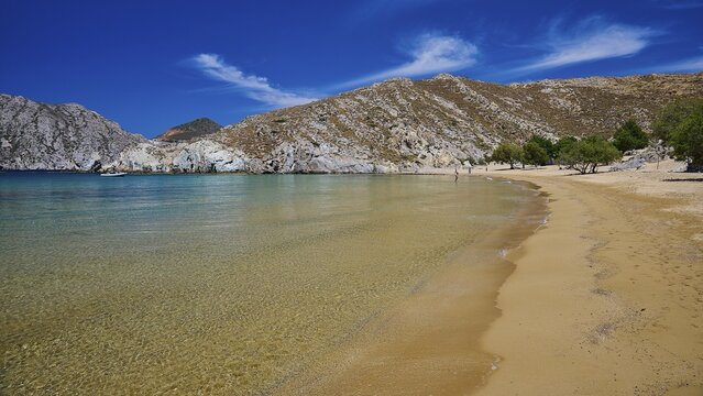 Extensive golden sandy beach with clear water, framed by rocks and trees under a bright blue sky, Psili Ammos Srand, Patmos, Dodecanese, Greek Islands, Greece