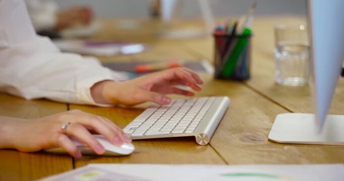 Businesswoman typing on wireless keyboard and using mouse at wooden office desk close up.