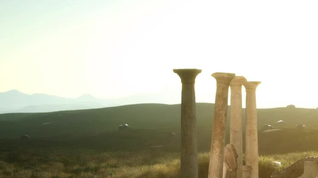 Four stone columns rise against a bright sky in an open area. These columns are remnants of an ancient structure, showing signs of weathering. The scene captures the beauty of history.