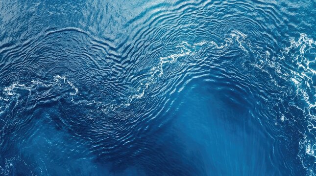 Waves roll across a deep blue ocean. The water surface displays dynamic, rippling patterns, reflecting light and creating a sense of movement.