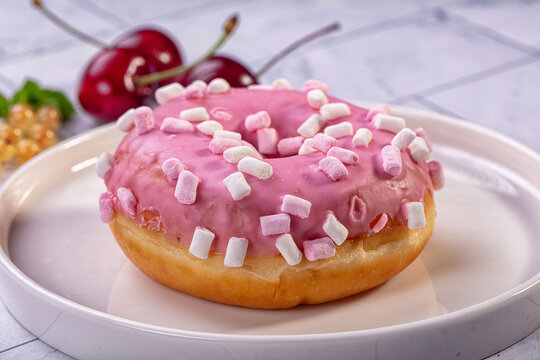Pink frosted donut with mini marshmallows and cherries on white plate