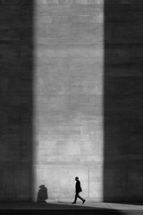 Obraz na płótnie Canvas Dramatic shadow play shows a person walking past a textured wall during the day with clear outlines of shadows cast on the surface