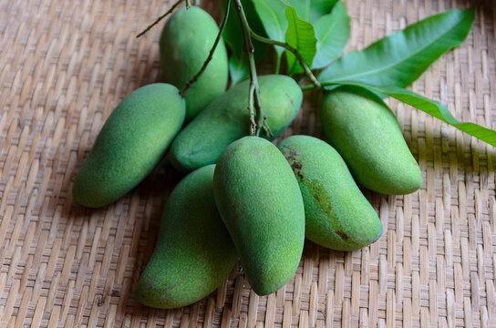 Fresh green mangoes with natural leaves arranged on a traditional bamboo basket, showcasing tropical fruit, organic harvest, and healthy food