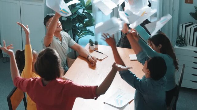 Top view of smart people throw paper and giving high five at meeting table with financial document and stock market analysis paper scattering around. Aerial view of team celebrate project. Symposium.