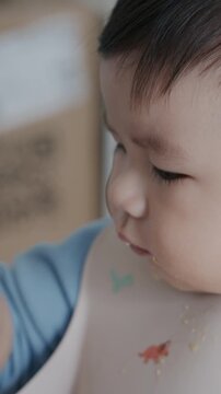 4K close up Cute Asian baby boy sitting in high chair and eating food with his hand at home.	