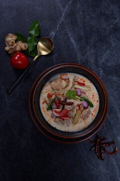 Tom Kha Gai or Thai Coconut Chicken Soup in black bowl on dark slate backdrop. Tom Kha Gai is Thailand cuisine dish with coconut milk, chicken, galangal, lemongrass, mushrooms, lime. Thai Food