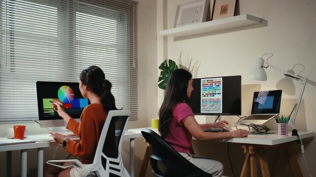 Two asian creative colleagues working together in a modern office. Graphic designers choosing colors from a swatch for a new project
