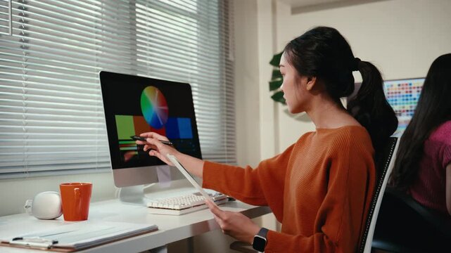 Professional female Asian video editor working on color grading and correction on her desktop computer, creating content in an office