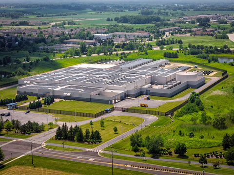 Aerial view of a AI industrial facility with solar panels on the roof, surrounded by green fields and parking lots