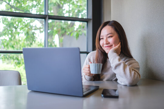 Portrait image of a woman drinking coffee while working on laptop computer