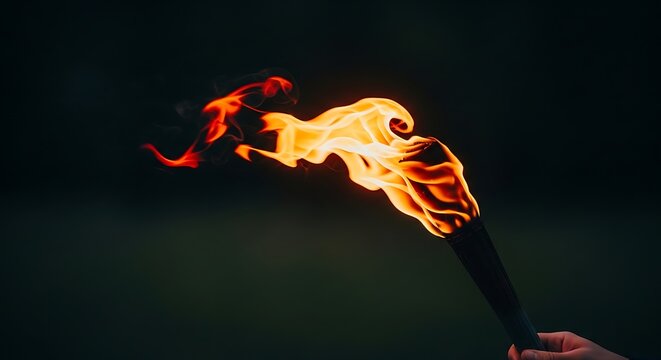 Hand holding a burning torch with bright orange flames in the darkness