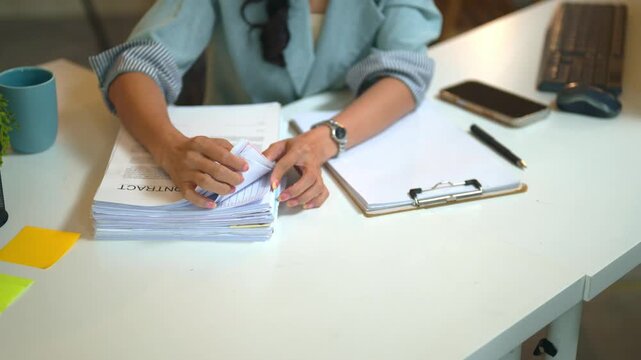 Businesswoman Reviewing Stack of Contract Documents at Office Desk with Clipboard and Smartphone