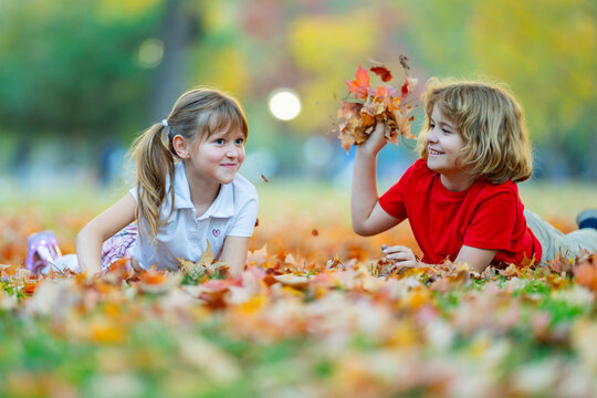 Autumn play with fallen leaves. Children enjoy outdoor fun. Leaves scatter near smiling kids. Play creates natural motion. Laughing children share joy. Friendship concept in fall park.