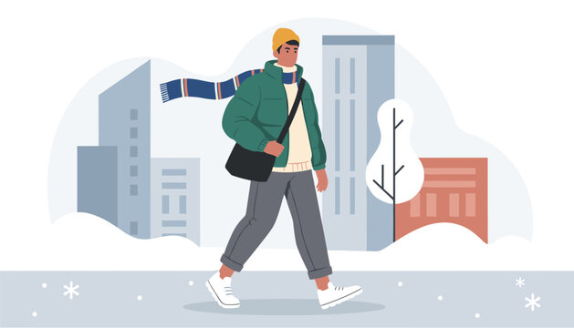 Young man in green warm puffer jacket and winter scarf walking down snowy city street on cold windy day.