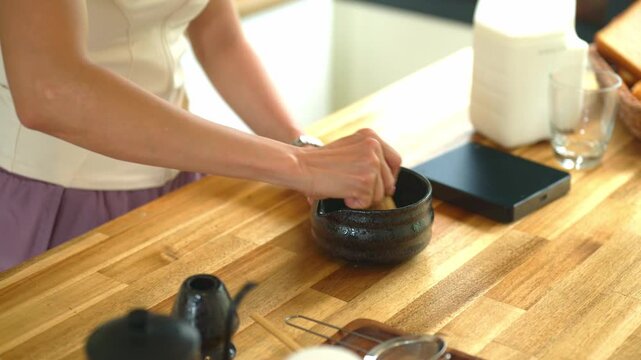 Closeup Whisking Matcha Green Tea in Traditional Black Bowl on Wooden Kitchen Counter