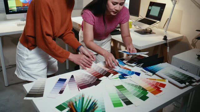 Two Asian female graphic designers collaborating on a new project. Colleagues choosing color swatches and palettes together in the office