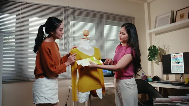 Young Asian fashion designer team checking color palettes for a new clothing collection. Professional stylists working together in a studio