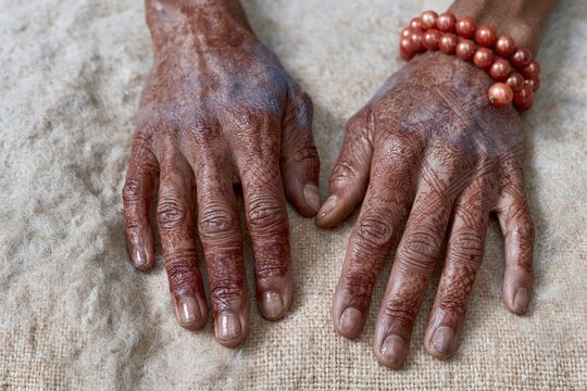 Detailed henna designs on womans hands resting on a beige woven surface with a coral beaded bracelet for Indian cultural tradition and bridal beauty