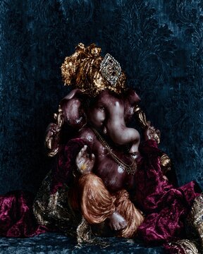 Ganesha idol with a golden gilded crown and magenta dhoti seated against a teal damask background for Ganesh Chaturthi festival celebrations