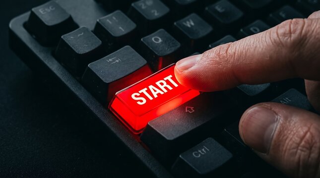 Human finger pressing glowing red start button on black computer keyboard symbolizing project launch and digital activation for technological business success and progress