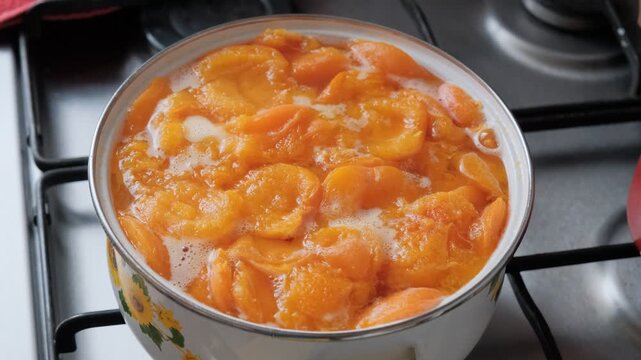 The pot of apricot compote is boiling on the stove.