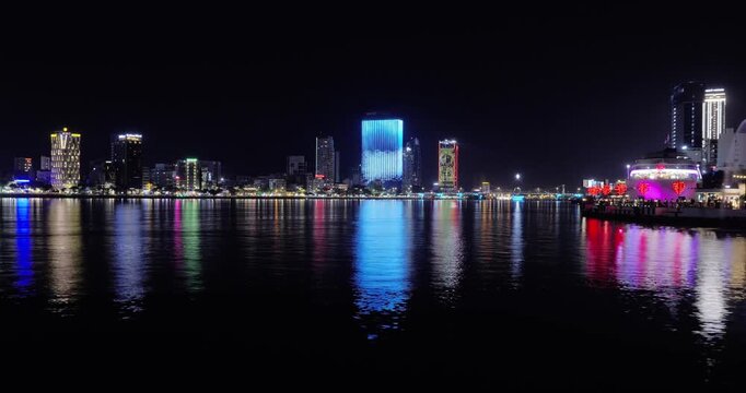 Night skyline of da nang city featuring vibrant neon lights reflected on river water surface.